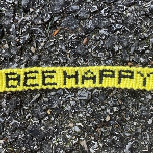 May include: A yellow knitted bracelet with the words "BEE HAPPY" woven in black.