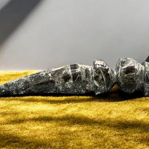 Puede incluir: Una escultura abstracta de piedra negra y verde. La escultura está tumbada sobre una superficie amarilla y peluda.