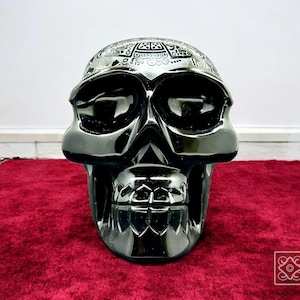 Puede incluir: Una escultura de calavera cromada brillante con intrincados patrones en la parte superior. La calavera está sobre una superficie de terciopelo rojo. Tiene cuencas oculares grandes y una mandíbula detallada. El logotipo de Inaro Mexico es visible.