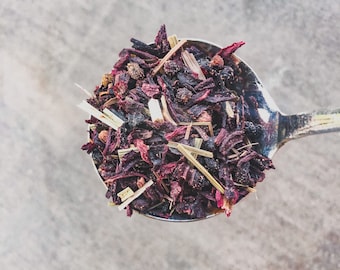 May include: A silver spoon filled with a blend of dried hibiscus flowers, lemongrass, and black peppercorns.