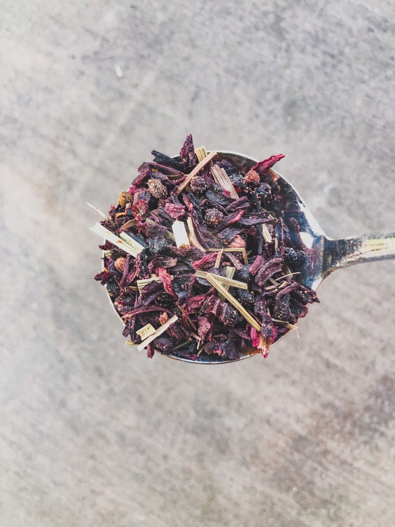 May include: A silver spoon filled with a blend of dried hibiscus flowers, lemongrass, and black peppercorns.