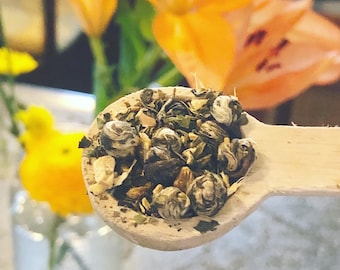 May include: A wooden spoon filled with loose leaf green tea. The tea is a blend of green tea leaves, white tea pearls, and dried flowers.