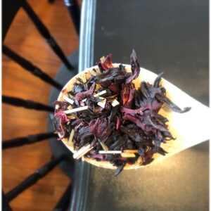 May include: A wooden spoon filled with dried hibiscus flowers, a common ingredient for herbal teas.