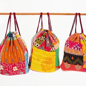 May include: Three colorful drawstring bags made of patchwork fabric. Each bag has a different pattern of bright colors and intricate stitching. The bags are hanging from a wooden dowel.