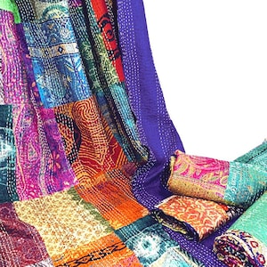 May include: A patchwork quilt featuring a vibrant array of multicoloured fabric squares with intricate floral and geometric patterns. The textile is accented with visible white running stitch embroidery and includes a solid purple border section.