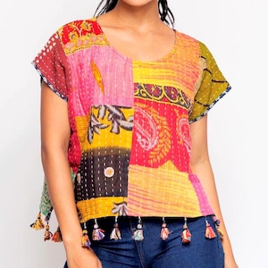 May include: A patchwork top with a V-neckline and short sleeves. The top features a variety of colorful fabric patches in shades of red, pink, yellow, and black. The bottom hem is adorned with small tassels. The top is made of a soft, lightweight material.