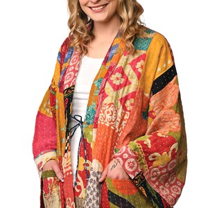 A vibrant patchwork kimono-style jacket featuring a fun mix of colors and patterns, including bright tones with floral, geometric, and abstract designs. The jacket has wide sleeves, a relaxed fit, and visible hand-stitching, creating a boho look.