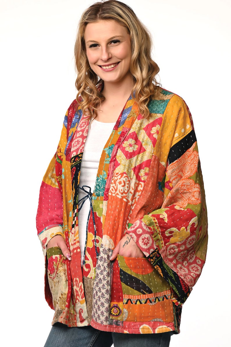 A vibrant patchwork kimono-style jacket featuring a fun mix of colors and patterns, including bright tones with floral, geometric, and abstract designs. The jacket has wide sleeves, a relaxed fit, and visible hand-stitching, creating a boho look.