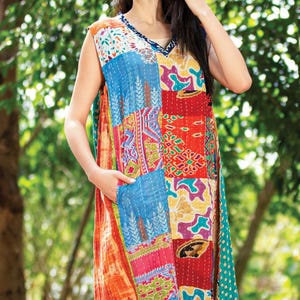 Puede incluir: Un vestido sin mangas de patchwork con cuello en V. El vestido presenta una vibrante mezcla de colores y patrones, incluyendo azul, rojo, naranja y verde. El vestido tiene un corte holgado y bolsillos laterales. La modelo sonríe y está de pie al aire libre.