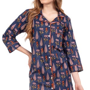 May include: Navy blue button-down sleep shirt with a floral pattern. The shirt features a repeating design of teardrop and flower shapes in shades of orange and pink. The collar and cuffs are trimmed with orange piping.