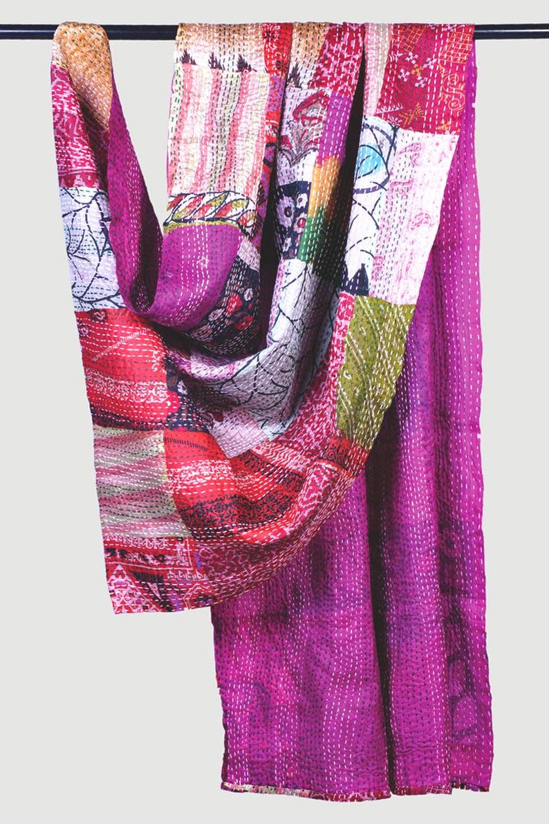 May include: A rectangular textile piece featuring a patchwork design of various fabric scraps in shades of magenta, pink, red, and white. The fabric is held together by visible white running stitches throughout, creating a textured, quilted appearance.