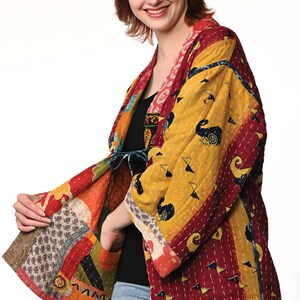 A vibrant patchwork kimono-style jacket featuring a fun mix of colors and patterns, including bright tones with floral, geometric, and abstract designs. The jacket has wide sleeves, a relaxed fit, and visible hand-stitching, creating a boho look.
