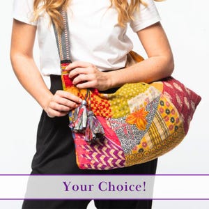 Puede incluir: Un bolso de hombro de patchwork colorido con una correa larga y un borla. El bolso está hecho de diferentes telas en tonos de rojo, amarillo, morado y verde.