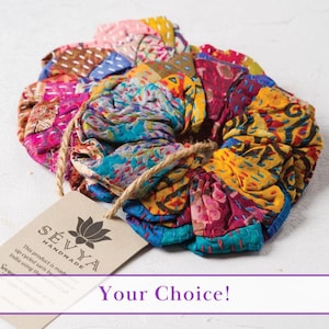 Puede incluir: Un scrunchie para el cabello de tela colorida hecho de saris reciclados. El scrunchie tiene forma de flor y presenta una variedad de colores y patrones. El texto en la etiqueta dice "SÉVYA HANDMADE This product is made from up-cycled saris by India using the"