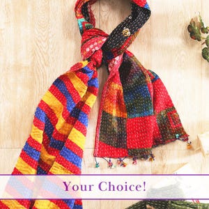 May include: A multi-colored scarf featuring a patchwork design with red, yellow, and blue stripes and blocks. The fabric is held together by visible white running stitches throughout the material, and the ends are finished with small, dangling tassels.