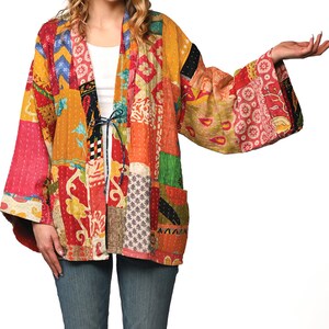 A vibrant patchwork kimono-style jacket featuring a fun mix of colors and patterns, including bright tones with floral, geometric, and abstract designs. The jacket has wide sleeves, a relaxed fit, and visible hand-stitching, creating a boho look.