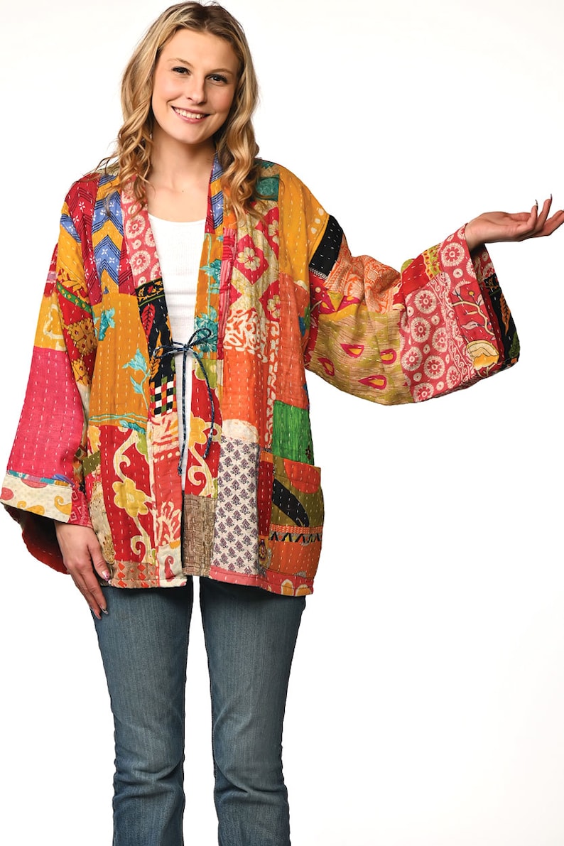 A vibrant patchwork kimono-style jacket featuring a fun mix of colors and patterns, including bright tones with floral, geometric, and abstract designs. The jacket has wide sleeves, a relaxed fit, and visible hand-stitching, creating a boho look.