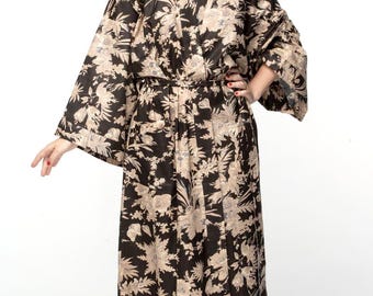 May include: A long, black kimono-style robe with a floral pattern in beige and tan. The robe has wide sleeves and a belted waist. The model is wearing the robe, standing against a white background.