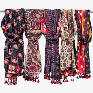 May include: Five rectangular scarves featuring kantha stitching and various patterns including grids with red circular motifs, floral designs, geometric swirls, and polka dots. Each scarf has small fabric tassels at the bottom edges.