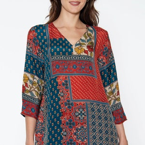 May include: A patchwork-style tunic top with a V-neck and three-quarter sleeves. The top features a mix of teal, red, and cream-colored floral and geometric patterns. The garment is made of a lightweight fabric and is worn with blue jeans.