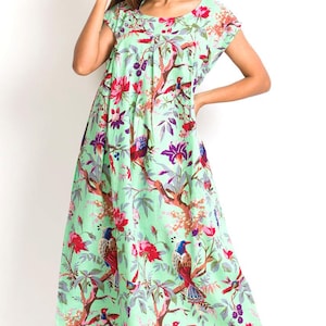 May include: A light green midi dress featuring a vibrant print of colorful birds, dark brown tree branches, and bright red and purple flowers. The garment has short sleeves, a round neckline, and a loose, flowing silhouette that falls below the knee.