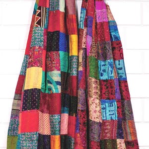 May include: Two baby carriers made from multicoloured patchwork fabric featuring various patterns and textures. Each carrier is suspended from a circular wooden ring at the top, showcasing a vibrant array of red, blue, yellow, and pink squares.