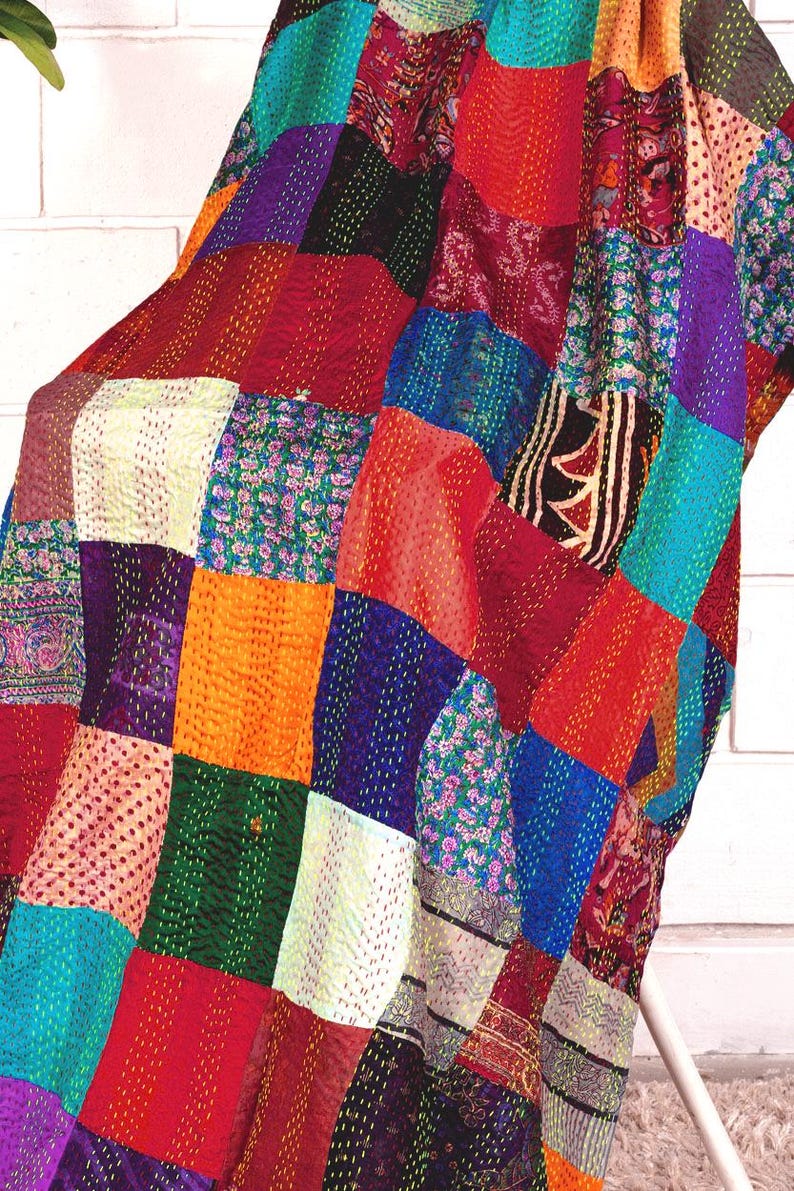 May include: A patchwork quilt featuring a variety of colourful fabric squares in shades of red, blue, orange, green, and purple. The textile displays intricate running stitch patterns throughout, creating a textured surface with diverse floral and geometric prints.