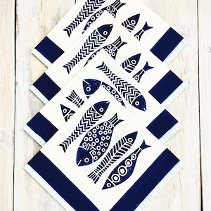 Peut inclure: Ensemble de quatre serviettes en coton blanc avec une bordure bleue et un motif de poisson bleu. Les poissons sont stylisés et ont un motif en zigzag sur leur corps.