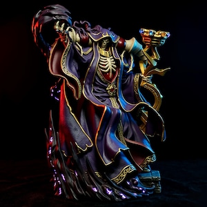 May include: A detailed figurine of a skeletal figure in a purple robe with gold trim, holding a staff and a dark orb. The figure has a skull face and is standing on a base with purple glowing accents. The background is dark.