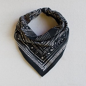 May include: A black and white bandana with a geometric pattern. The square scarf is folded and tied at the top, displaying a repeating design of dots and lines. The bandana is made of a soft fabric and is suitable for various uses.