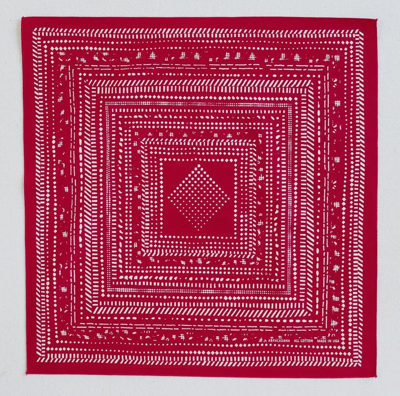 May include: Red square bandana with a white geometric pattern. The design features concentric squares with dotted and dashed lines, and a central diamond shape. The bandana is made of cotton and has text that reads "ALL COTTON MADE IN USA".