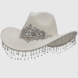 May include: A white cowboy hat with a large rhinestone embellishment and a fringe of rhinestones around the brim.