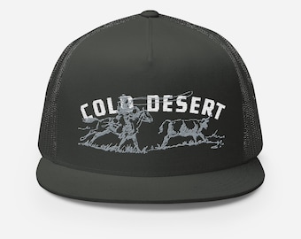 May include: A dark green trucker hat with a white embroidered design of a cowboy riding a horse and a cow. The text "COLD DESERT" is embroidered in white above the design.