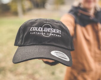 Puede incluir: Gorra de béisbol negra con un logotipo bordado que dice "Colo Desert Clothing Company".