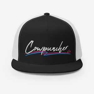 Pu&ograve; includere: Cappellino da camionista nero e bianco con la scritta "Cowpuncher" ricamata in corsivo bianco. Il design include linee blu e rosa sotto il testo e un piccolo simbolo a forma di cuore. Il cappellino ha un retro in rete.