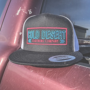 May include: Black and white trucker hat with a red and blue embroidered logo that says "COLD DESERT CLOTHING COMPANY".