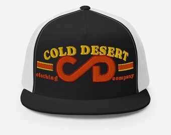 May include: Black and white trucker hat with the text "COLD DESERT clothing company" in gold and orange embroidery. The hat features a black brim and a white mesh back.