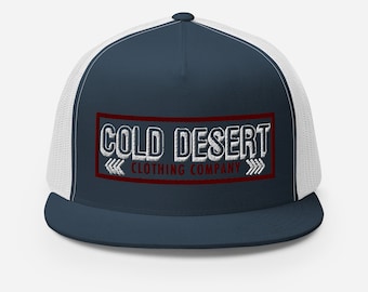 May include: A navy blue and white trucker hat with a red border around a white embroidered logo that says "COLD DESERT CLOTHING COMPANY" with arrows on either side.