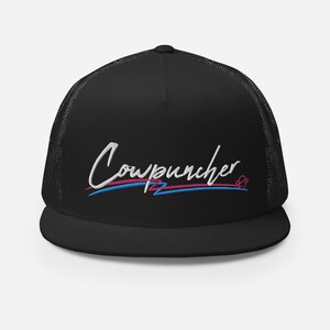 Pu&ograve; includere: Cappellino da camionista nero con retro in rete e visiera piatta. Il cappello presenta la scritta ricamata "Cowpuncher 12" in corsivo bianco, con accenti blu e rosa. Un disegno a forma di cuore &egrave; accanto al testo.