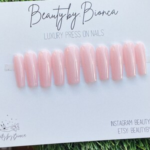 May include: A set of ten light pink coffin-shaped press-on nails. The nails are arranged in two rows on a white card with the text "Beauty by Bianca" and "Luxury Press On Nails".