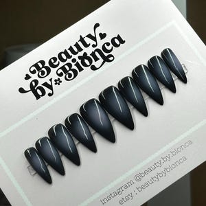 May include: A set of ten black stiletto false nails with a subtle shimmer finish. The nails are arranged on a white card with the text "Beauty by* Bionca" and social media information.