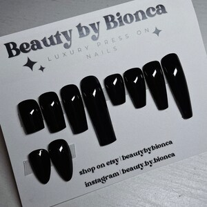 May include: A set of glossy black press-on nails in various shapes, including coffin and oval. The card reads "Beauty by Bionca, Luxury Press On Nails." The Etsy and Instagram shop names are also visible.
