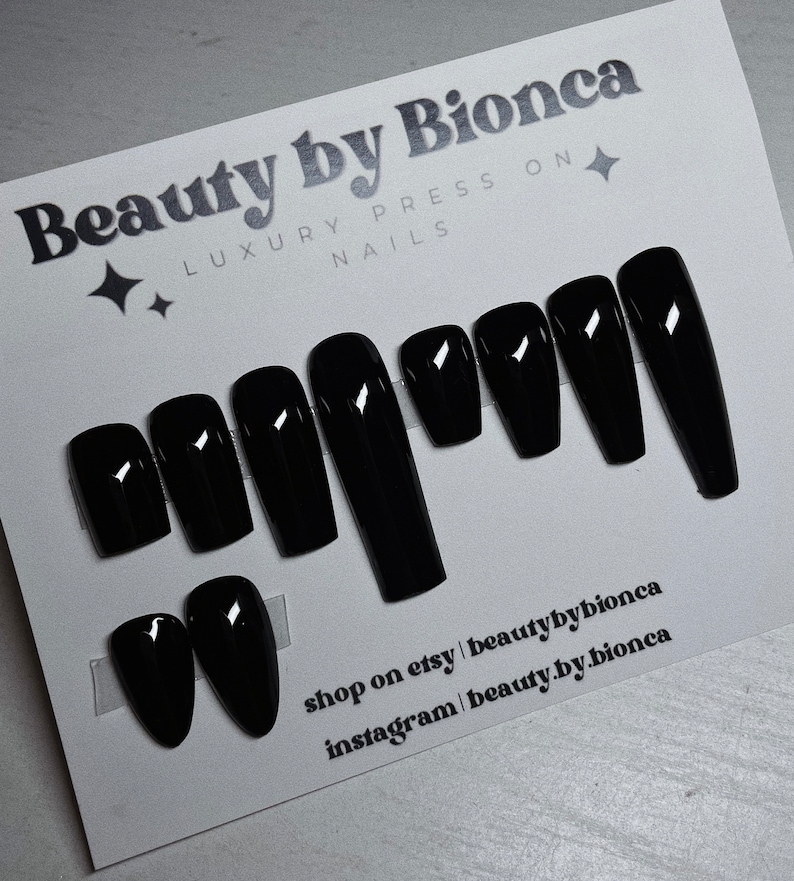 May include: A set of glossy black press-on nails in various shapes, including coffin and oval. The card reads "Beauty by Bionca, Luxury Press On Nails." The Etsy and Instagram shop names are also visible.