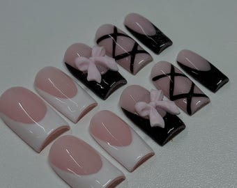May include: A set of ten artificial nails in various designs. Some nails feature a pink and white French tip, while others have a black base with pink bow accents or crisscross designs. The nails are arranged on a white surface.