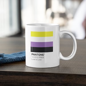 May include: White ceramic mug with a yellow, purple, and black stripe design. The mug has the text "PANTONE® 14-2012 PRIDE Love is Love" printed on the bottom.
