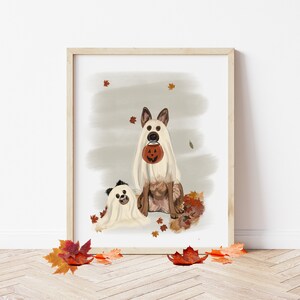 Pu&ograve; includere: Due cani vestiti da fantasmi per Halloween. Il cane pi&ugrave; grande tiene una piccola zucca arancione. I cani sono seduti su un letto di foglie autunnali.