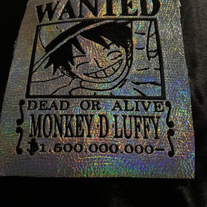May include: A holographic wanted poster with a black and white illustration of a cartoon character with a straw hat. The text on the poster reads "WANTED DEAD OR ALIVE MONKEY D. LUFFY $1,500,000,000"