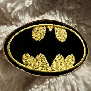 May include: A black and gold embroidered patch featuring the Batman logo.