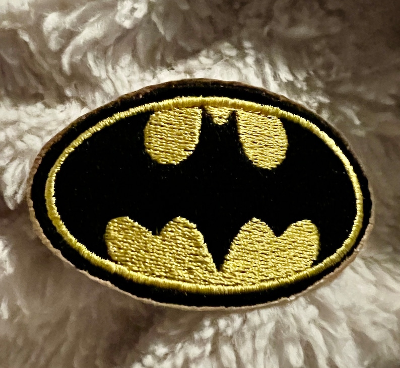 May include: A black and gold embroidered patch featuring the Batman logo.
