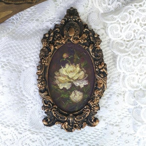 May include: A small oval painting of white peonies in a dark brown ornate frame. The frame is gold-gilded and has a detailed design.
